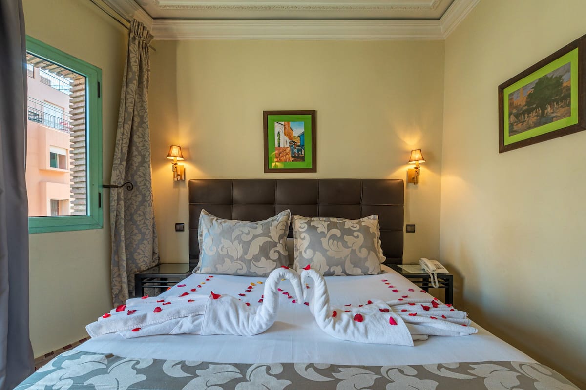 A hotel room with a bed, two pillows, a nightstand with a phone, and a painting on the wall.