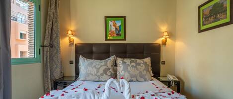 A hotel room with a bed, two pillows, a nightstand with a phone, and a painting on the wall.