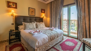 A hotel room with a large bed, two bedside lamps, a nightstand, a red and white patterned rug, and a balcony with curtains. - Hotel Le Caspien (Marrakech)