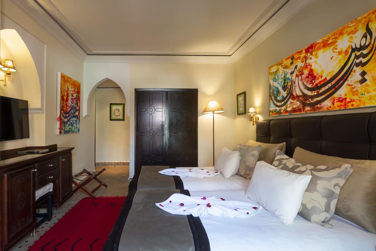 A hotel room with two beds, a TV, a desk, and a red carpet.