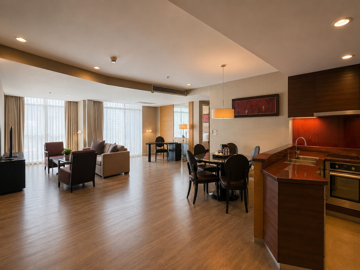 A hotel room with a dining area, a sofa set, a desk, and a kitchen area.