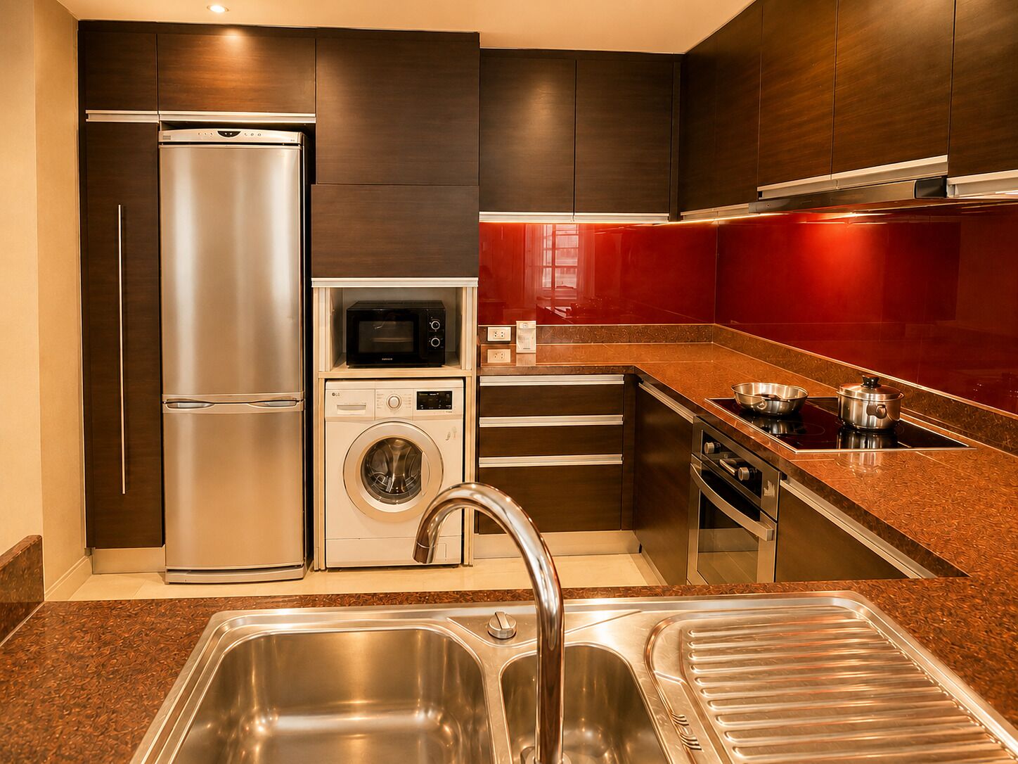A modern kitchen with stainless steel appliances, a built-in washer, and a red backsplash.