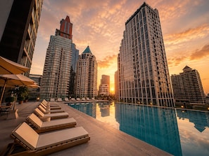 A rooftop pool with lounge chairs, surrounded by high-rise buildings and a sunset sky. - Urbana Sathorn Hotel (Bangkok)