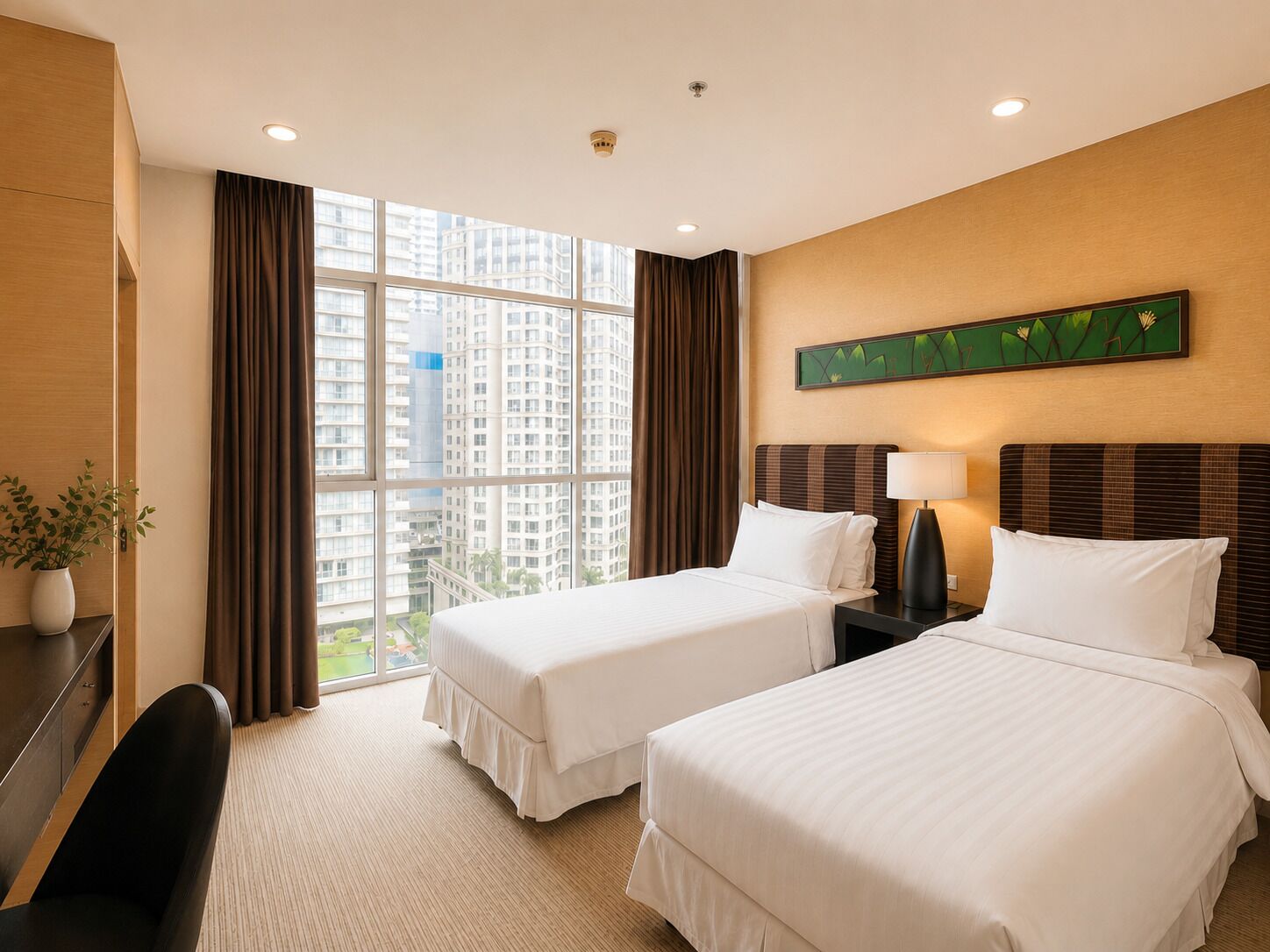 A hotel room with two beds, a desk, a chair, a potted plant, and a large window with a city view.