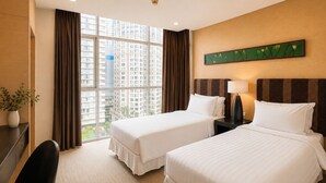 Ein Hotelzimmer mit zwei Betten, einem Schreibtisch, einem Stuhl, einer Topfpflanze und einem großen Fenster mit Blick auf die Stadt.