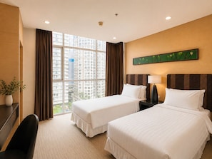 A hotel room with two beds, a desk, a chair, a potted plant, and a large window with a city view. - Urbana Sathorn Hotel (Bangkok)