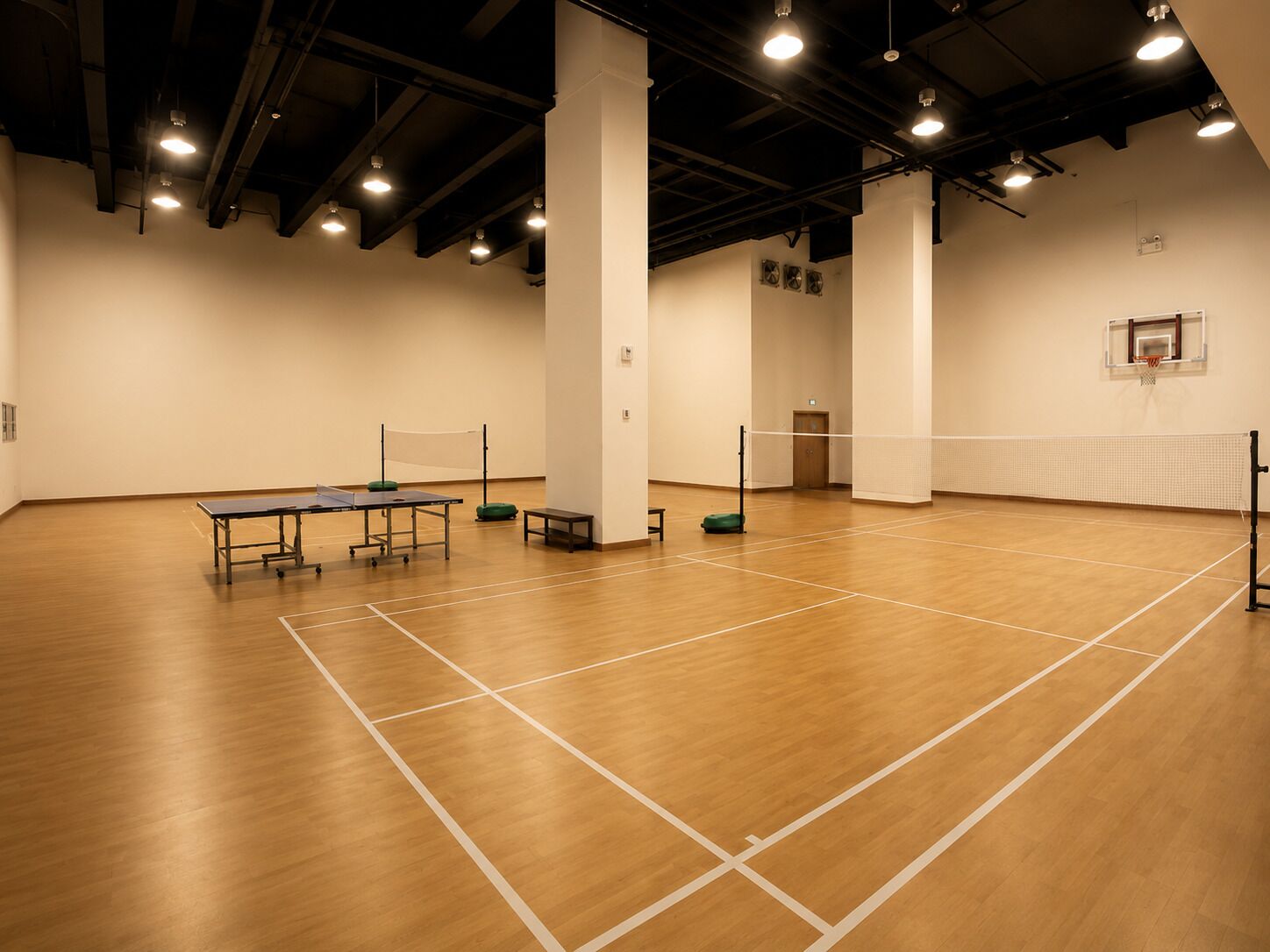 A spacious indoor sports hall with a ping pong table, a volleyball net, and a basketball hoop.