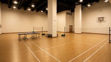 A spacious indoor sports hall with a ping pong table, a volleyball net, and a basketball hoop.
