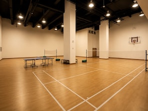 Een ruime sporthal met een tafeltennistafel, een volleybalnet en een basketbalring.
