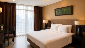 Ein Hotelzimmer mit einem großen Bett, zwei Nachttischlampen, einem Schreibtisch mit Stuhl und einem fensterbepflanzten Fenster.