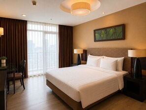 A hotel room with a large bed, two bedside lamps, a desk with a chair, and a window with curtains. - Urbana Sathorn Hotel (Bangkok)