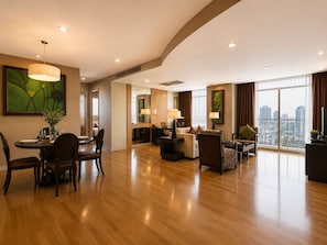 Une chambre d’hôtel spacieuse comprenant un coin repas, un salon et une grande fenêtre donnant sur la ville.