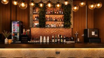 A bar area with a wooden counter, shelves of bottles, and hanging light fixtures.