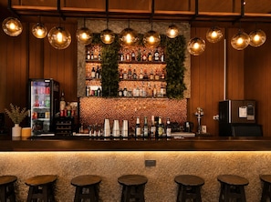 A bar area with a wooden counter, shelves of bottles, and hanging light fixtures.