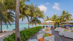 A beachside lounge area with white wicker furniture, green and orange cushions, and a view of the ocean.