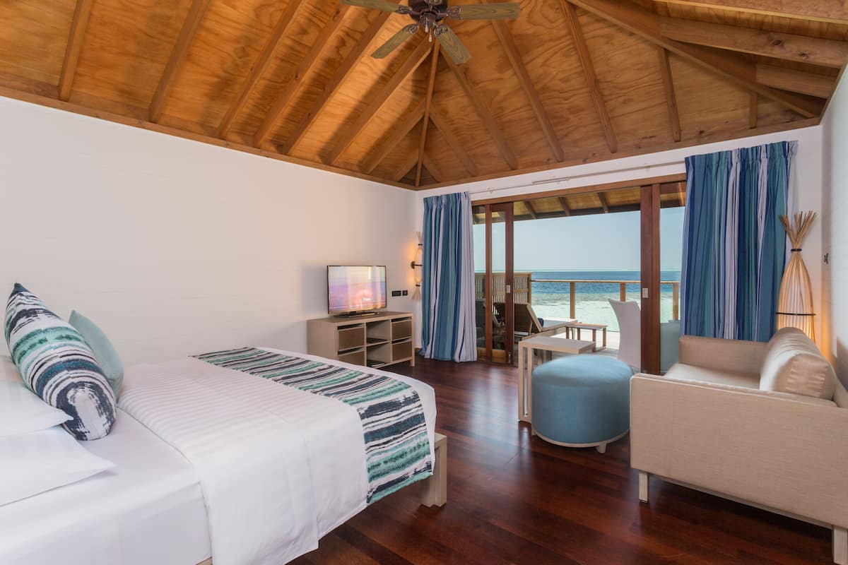 A room with a bed, a sofa, a TV, and a view of the ocean.