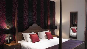 Ein Hotelzimmer mit Himmelbett, zwei Nachttischlampen, einem großen Spiegel und Wandpapier mit Muster.