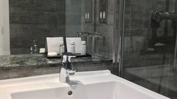 Et moderne badeværelse med en hvid vask, en brusekabine i glas og en bordplade i marmor.