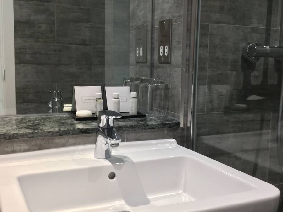 Et moderne badeværelse med en hvid vask, en brusekabine i glas og en bordplade i marmor.