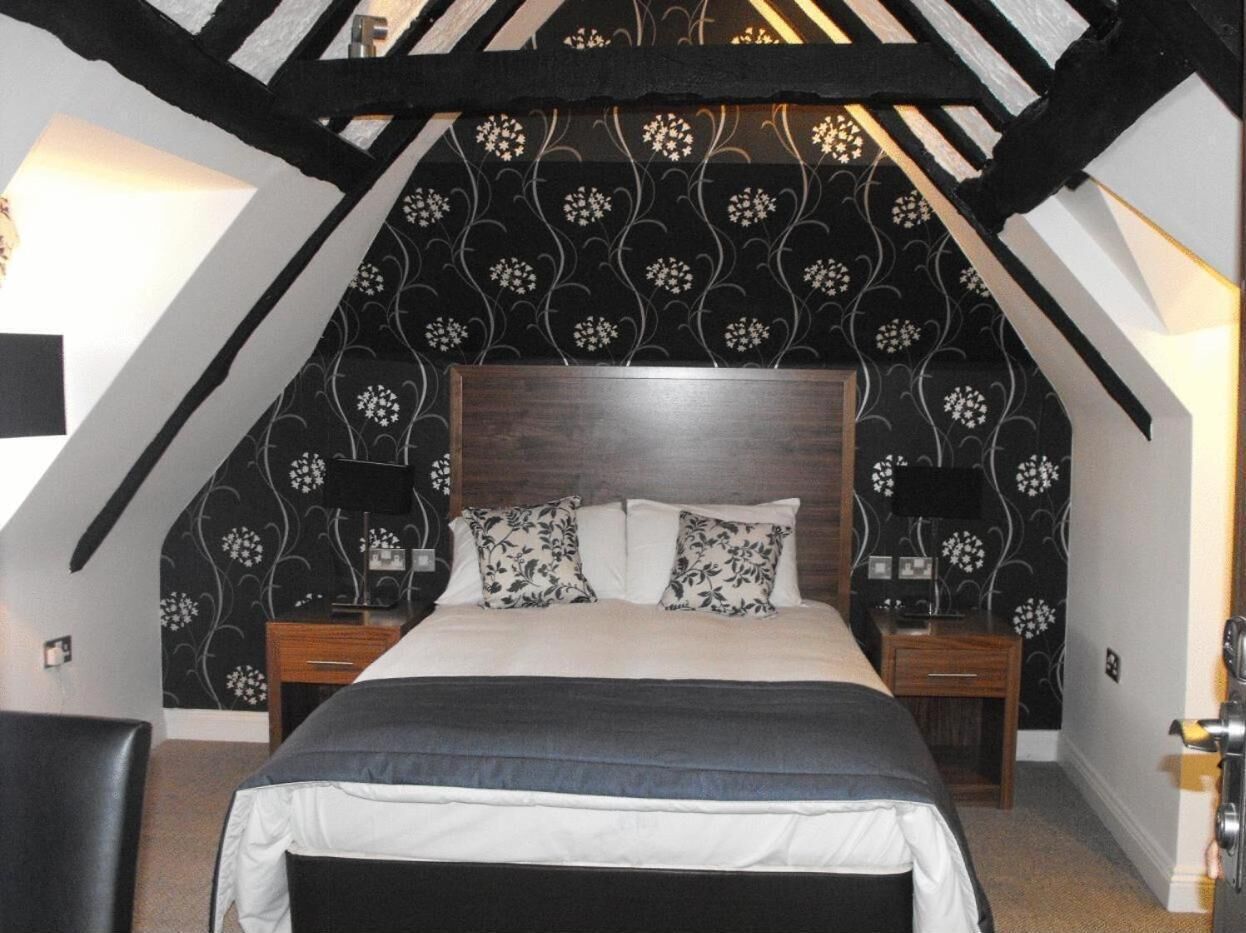 Una camera da letto con una testiera in legno scuro, un letto con biancheria da letto a fiori bianchi e scuri, due comodini con lampade e una carta da parati a motivi bianchi e neri.