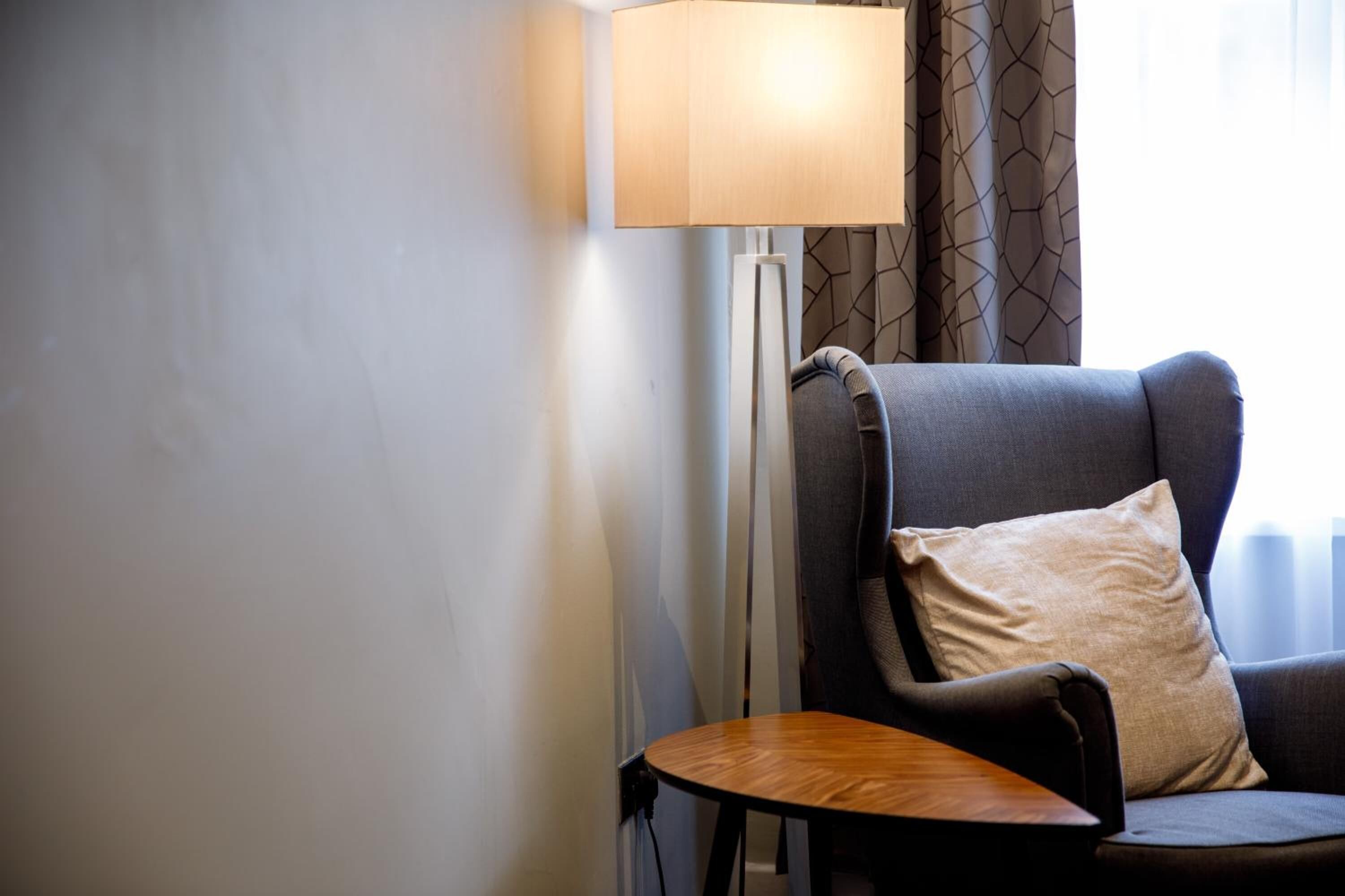 A modern room with a grey armchair, a small wooden side table, and a floor lamp.
