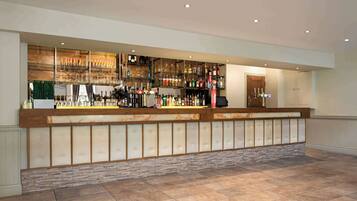 A bar area with a long counter, shelves with bottles and glasses, and a door to the right.