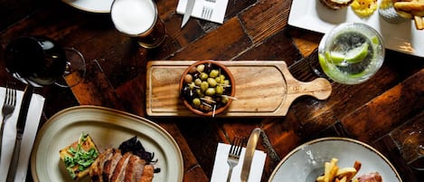 Une table à manger avec différents plats, notamment un steak, des frites et un bol d’olives.