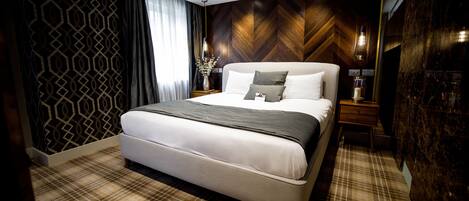 A modern bedroom with a large bed, a wooden herringbone wall, a patterned carpet, and a nightstand with a lamp.