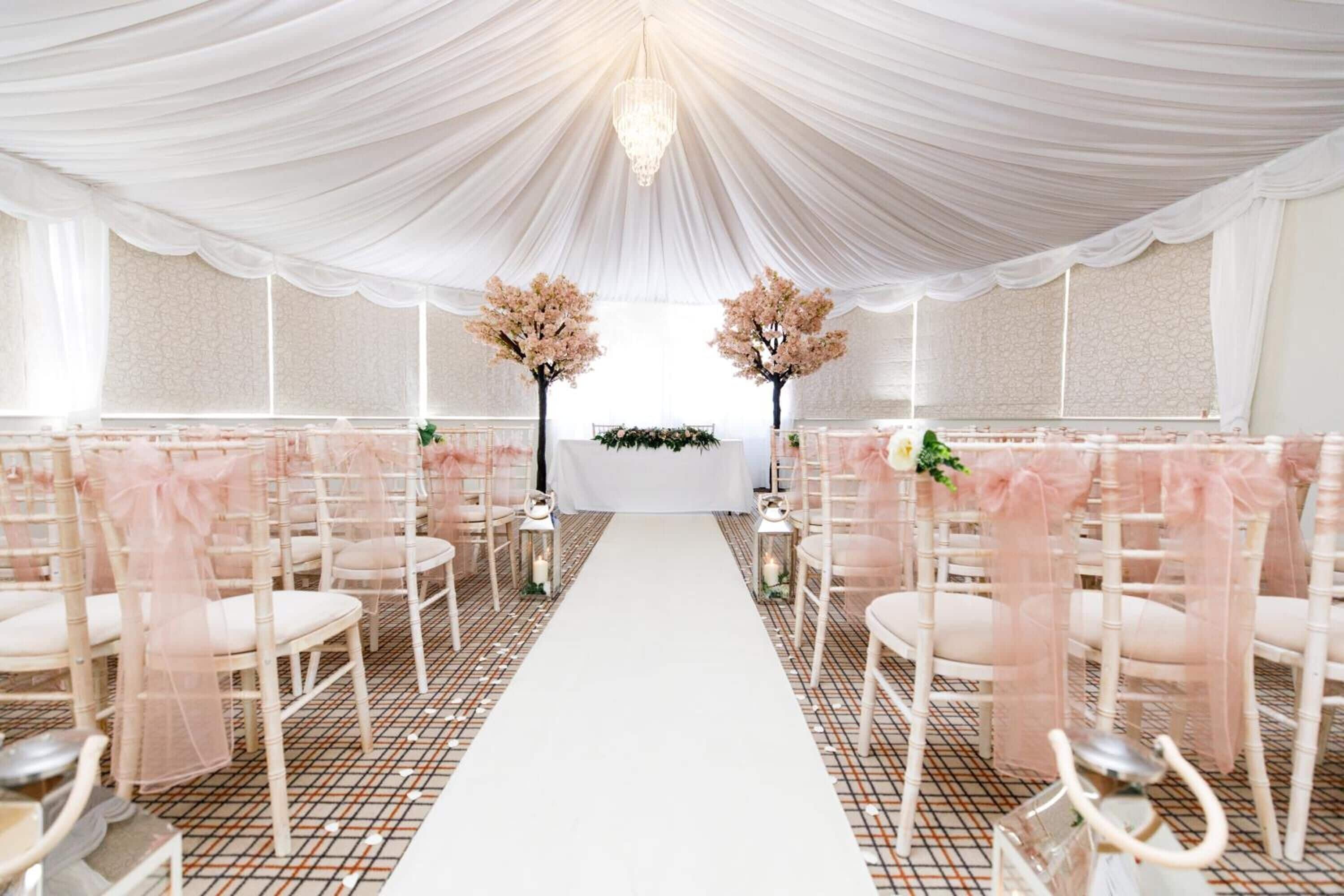 A wedding ceremony setup with white chairs, a white aisle, and a chandelier.