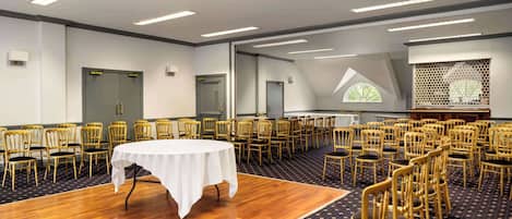 Un salón de conferencias con una mesa redonda, filas de sillas y una alfombra estampada.