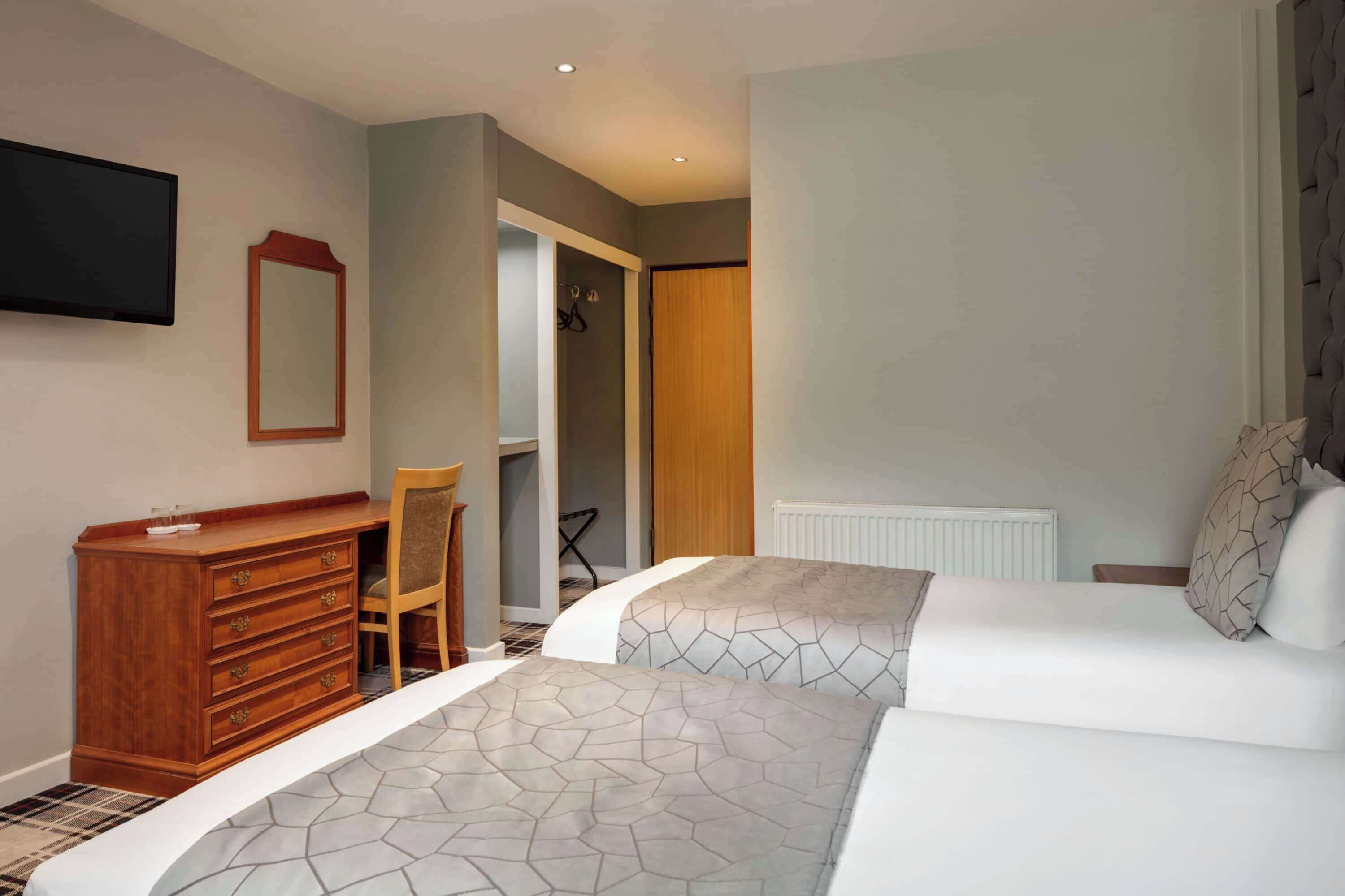 Een slaapkamer met twee bedden, een houten dressoir, een stoel, een spiegel en een kledingkast.