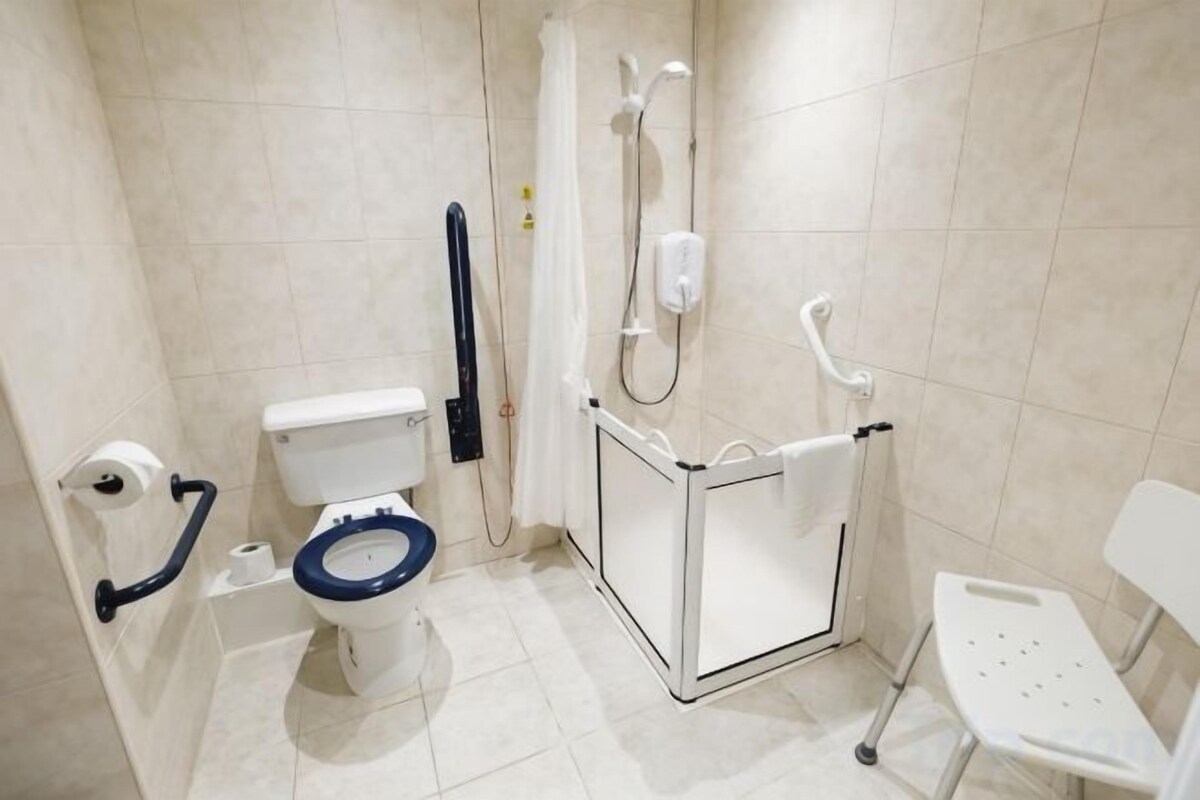 Un baño con inodoro, ducha y barras de apoyo.