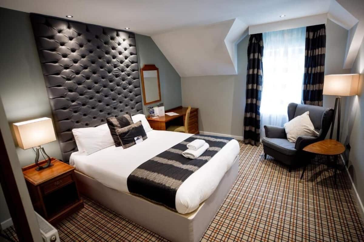 A hotel room with a large bed, a desk, a chair, and a window with curtains.