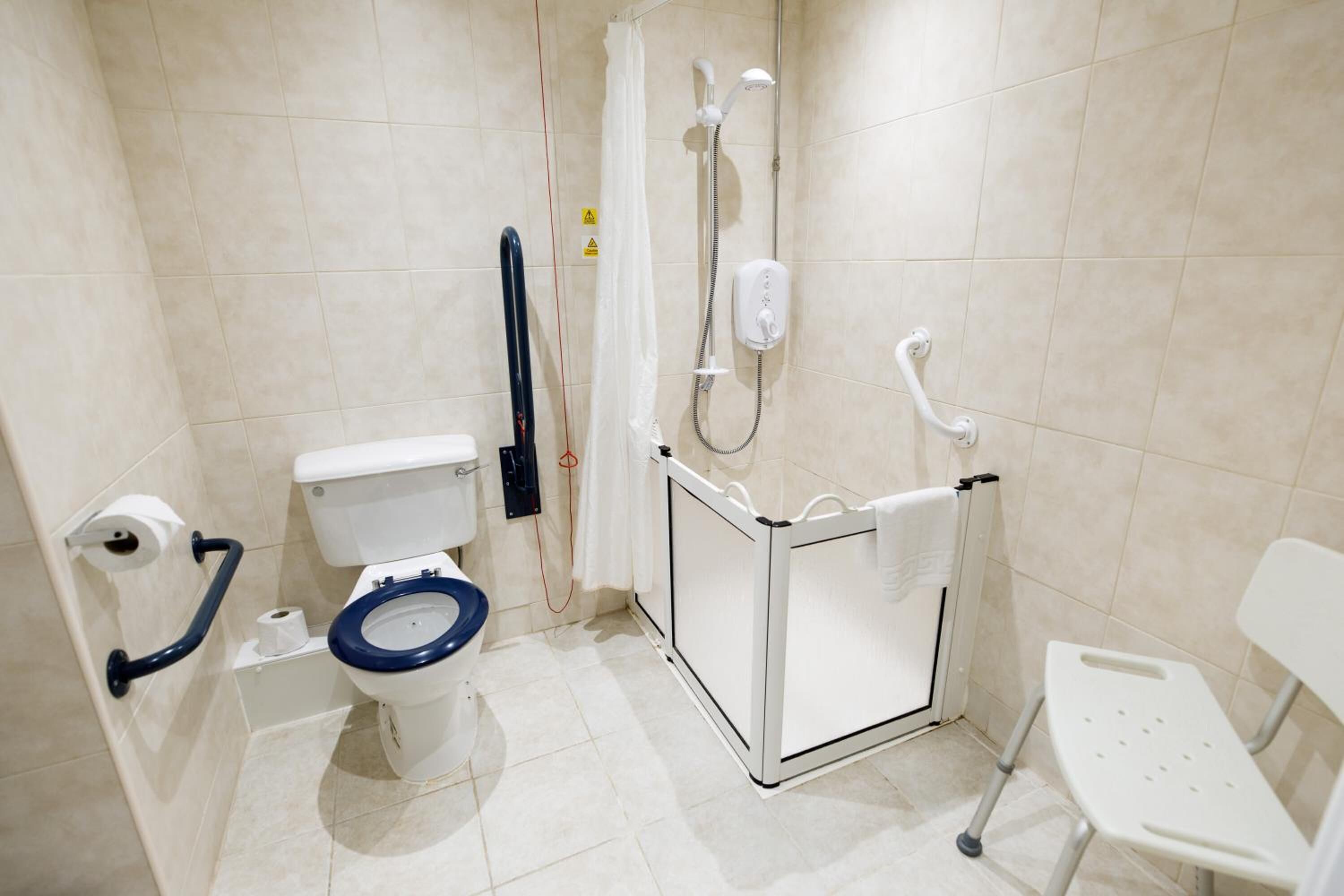Un baño pequeño y moderno con inodoro, ducha y barras de apoyo.