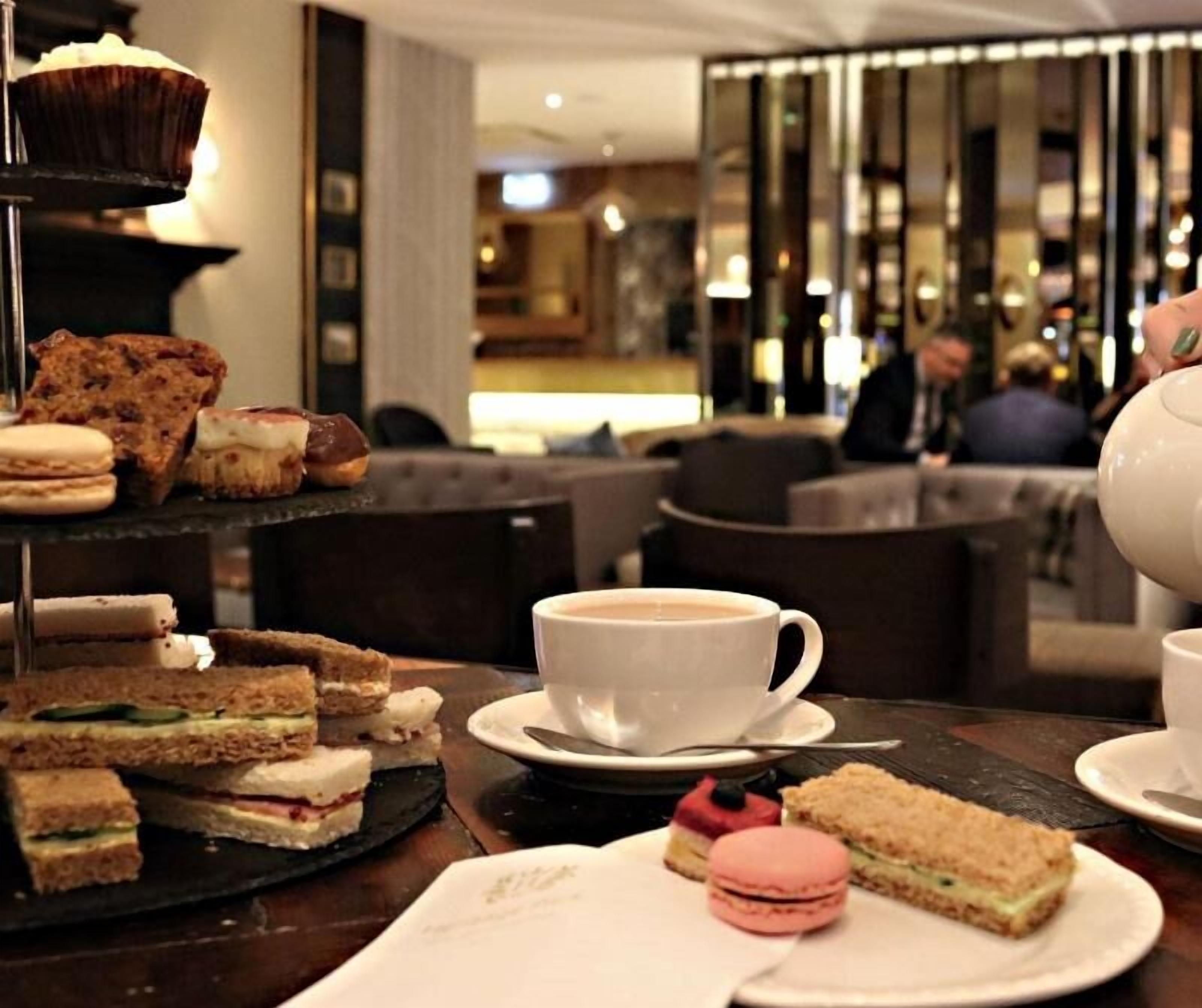 A table with sandwiches, macarons, and a cup of coffee in a cafe setting.