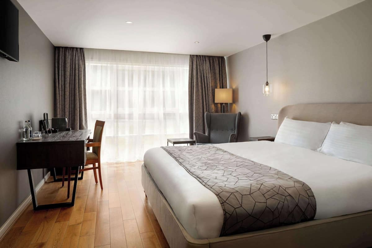 A hotel room with a bed, a desk, a chair, a lamp, and a TV.