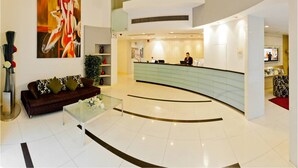 A modern lobby with a reception desk, a large abstract painting, a sofa, and a coffee table. - Citadines Xinghai Suzhou (Suzhou)