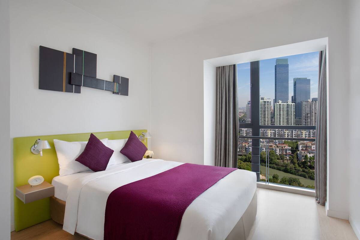 A modern hotel room with a large bed, a city view, and a minimalist decor.