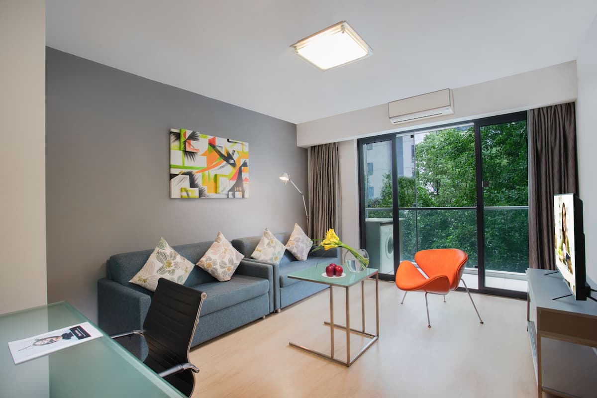 A modern living room with a grey sofa, a glass coffee table, a black office chair, and a bright orange chair.