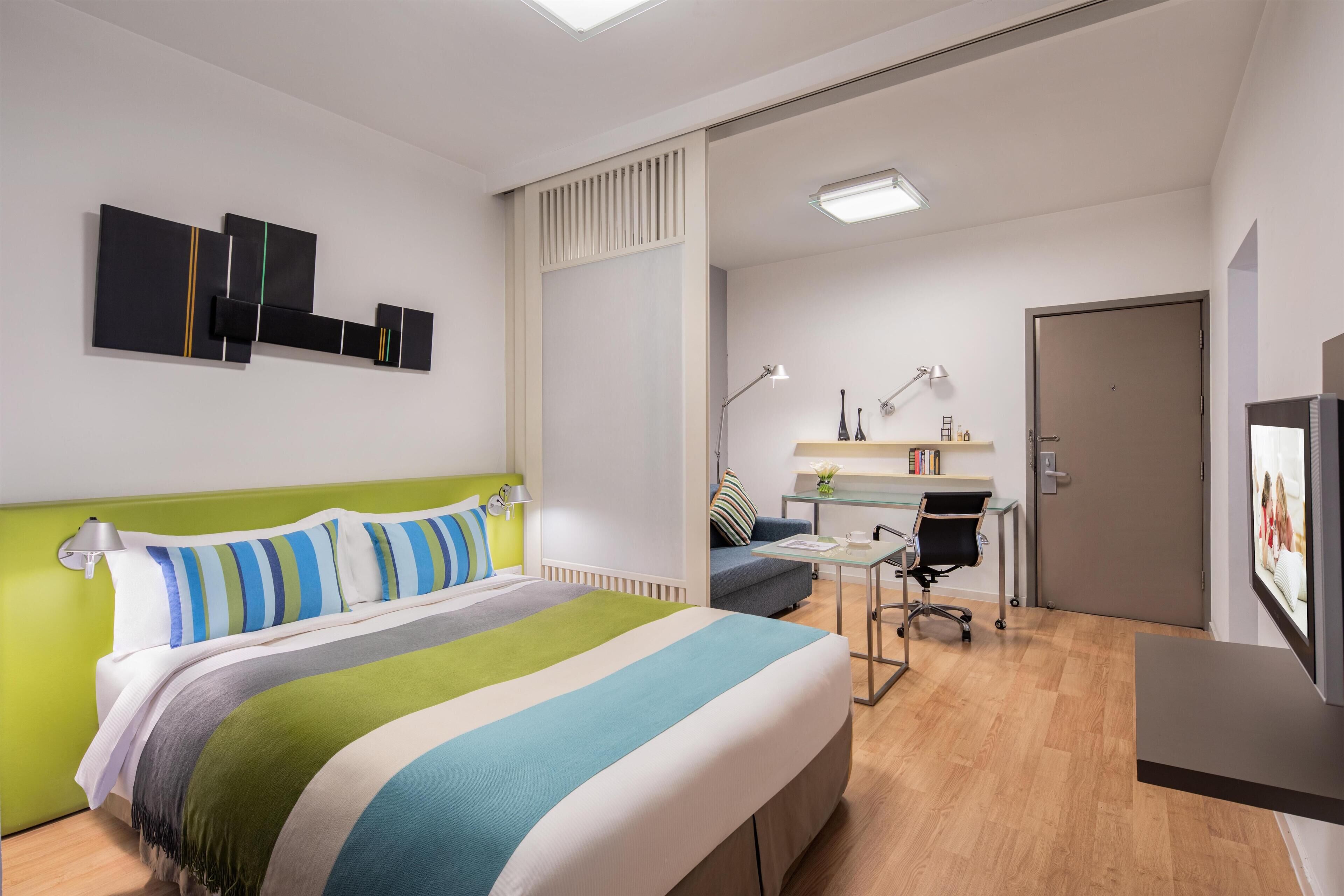 A modern hotel room with a bed, desk, and seating area.