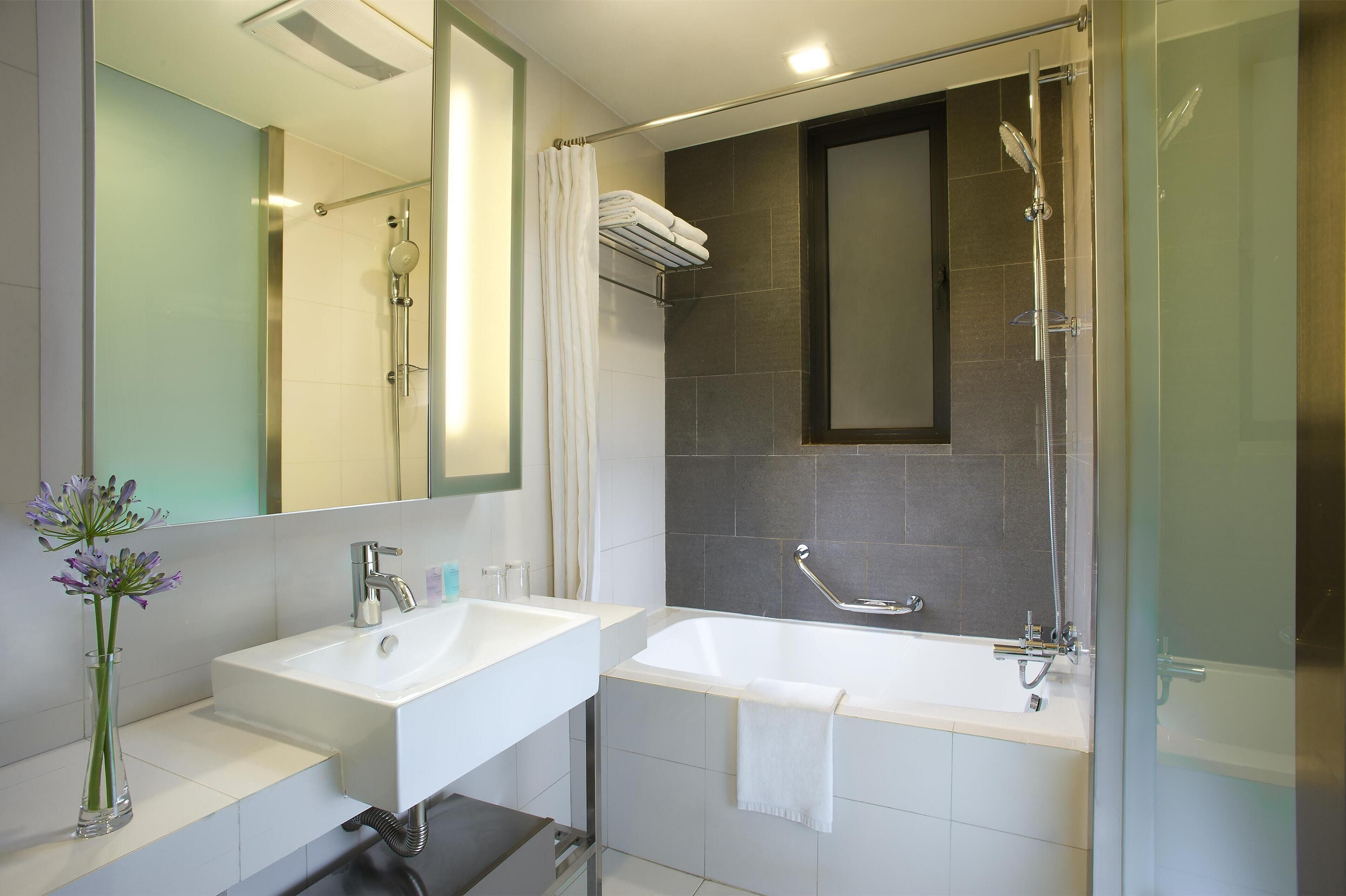 Un baño moderno con ducha envuelta en vidrio, un lavamanos blanco y un espejo grande.