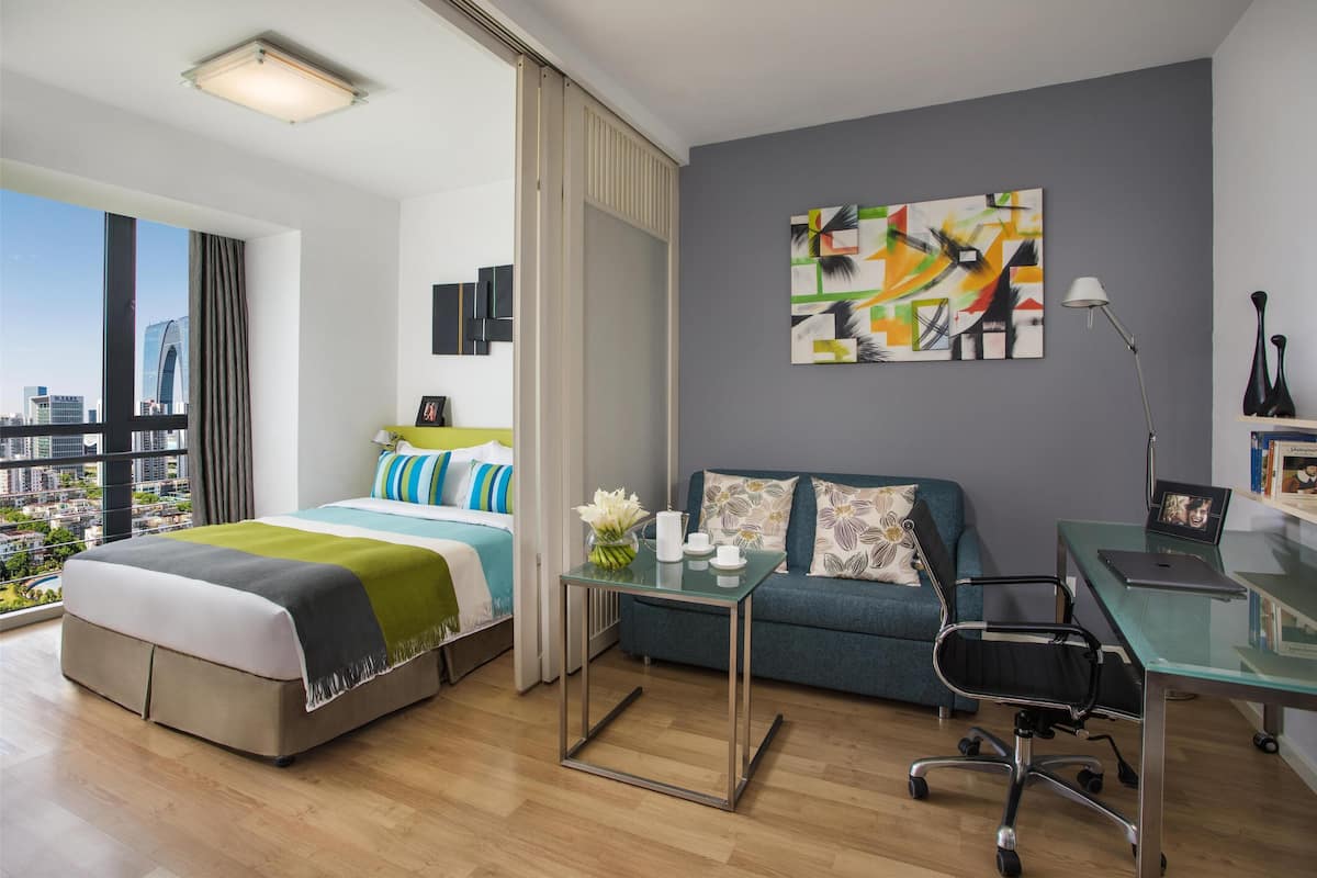 A modern hotel room with a large bed, a sofa, a desk, and a view of the city.