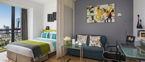 Habitación de hotel moderna con una cama grande, un sofá, un escritorio y vistas a la ciudad.