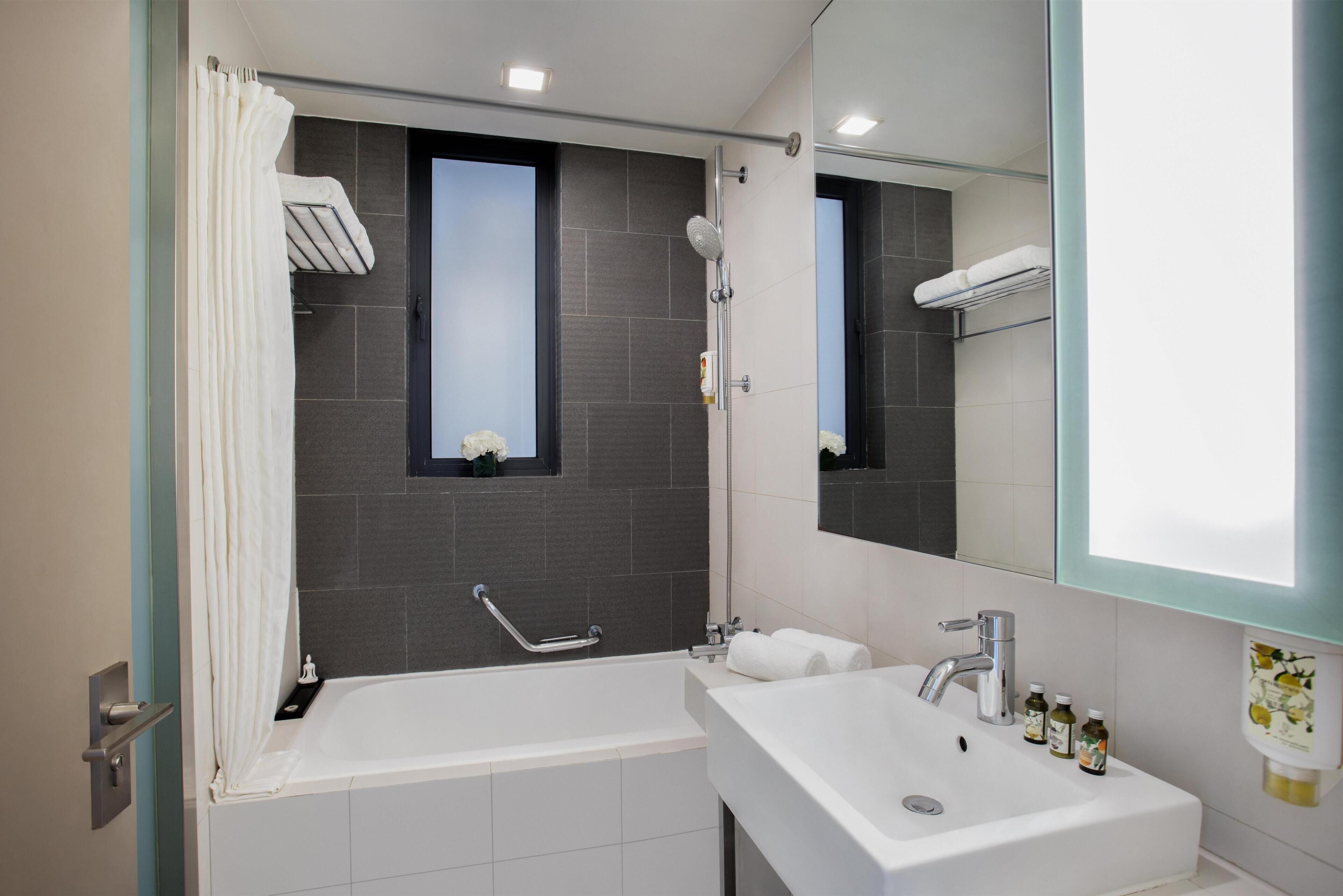 A modern bathroom with a bathtub, a sink, a shower, and a window.