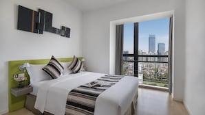 A modern hotel room with a large bed, a nightstand, a green accent wall, and a city view through large windows. - Citadines Xinghai Suzhou (Suzhou)