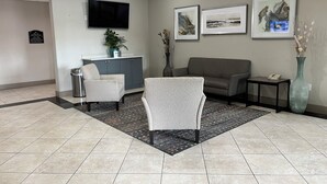 A reception area with a flat-screen TV, a potted plant, a grey sofa, a small table with a phone, and a vase with dried flowers. - Best Western Cleveland Inn & Suites (Cleveland)