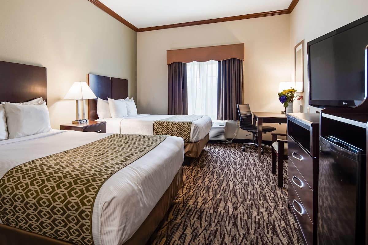 A hotel room with two beds, a desk, a television, and a large window with curtains.