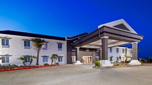 Una entrada de hotel moderna con un paseo techado, palmeras y cielo despejado.