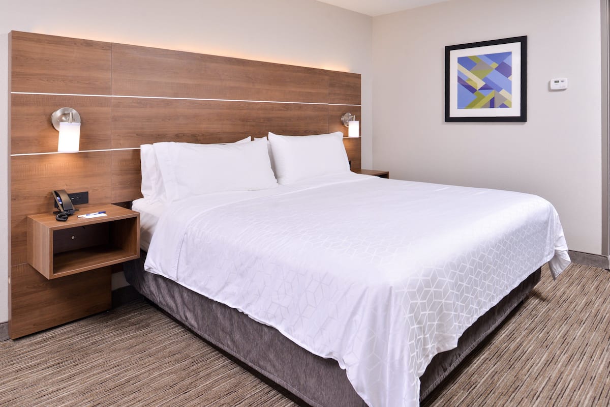 A hotel room with a large bed, wooden headboard, bedside tables, and a framed picture on the wall.