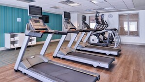 A fitness center with treadmills, exercise bikes, and a television screen.